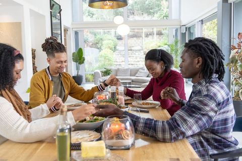 African american family holding hands and praying together at sunlit modern dining table