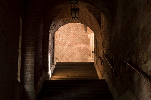 This photo captures an old brick arched staircase leading upwards towards light, creating a mysterious and historical atmosphere. Simple yet evocative. Perfect for illustrating concepts of history, transition, journey, or exploring ancient buildings. Suitable for educational materials, travel-related content, and architectural studies.
