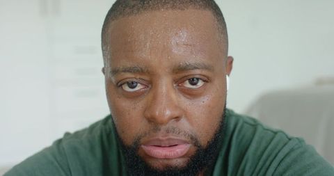 Sweating african man wearing earbud and green shirt, closeup tired portrait