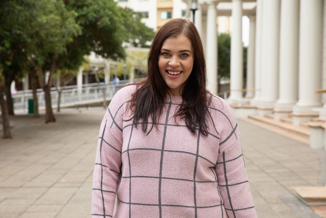 Portrait of an attractive curvy Caucasian woman out and about in the city streets during the day, looking to camera and smiling with the columns of a historical building in the background