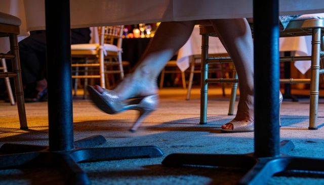 Seated woman slipping silver heels under banquet table, glamorous reception ambience