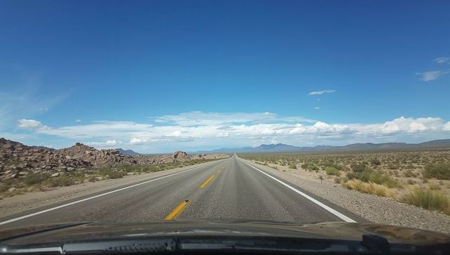 Endless desert highway stretching toward distant mountains from driver front perspective