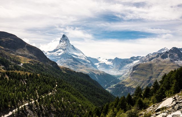 Picturesque view of the Matterhorn mountain surrounded by lush green valleys and forests. Ideal for travel brochures, nature documentaries, and promotional materials for Switzerland tourism. Perfect for outdoor adventure advertising, showing natural beauty, and conveying serenity and grandeur of the scenic highlands.