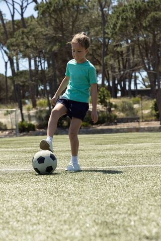 Young girl practicing soccer ball control and balancing on sunny turf field