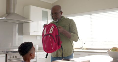 Grandfather Assisting Grandson with Schoolbag in Kitchen