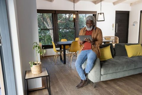 Senior african american man sitting on sofa arm using tablet in modern bright living room