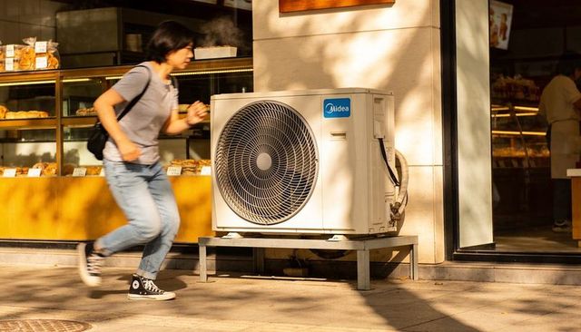 Pedestrian passing bakery storefront with visible midea air conditioning unit on sidewalk