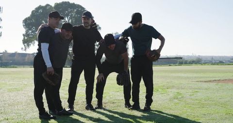 Five baseball teammates huddling on sunlit field during golden hour showcasing teamwork