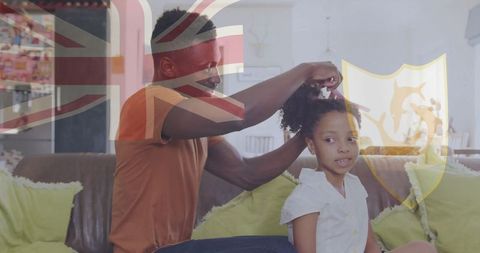 A father attentively grooms his daughter's curly hair on a sofa with a subtle UK flag overlay. This Nurturing Scene is Ideal for exploring themes surrounding family bonding, domestic life, and father-daughter relationships, with an added cultural touch with the Union Jack in the background.