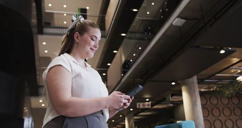 Businesswoman standing in modern office lobby using smartphone