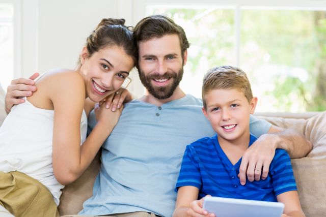 Portrait of parents and son sitting on sofa with arm around at home