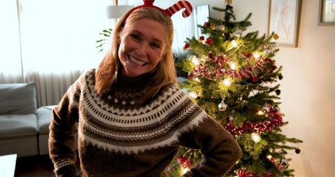 Senior Woman Wearing Holiday Sweater Standing by Lit Christmas Tree