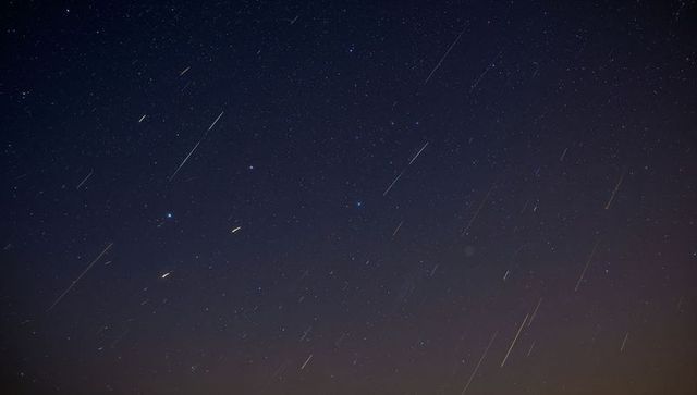 Meteor Shower Streaking Across Starfield Over Rural Horizon With Faint Orange Glow