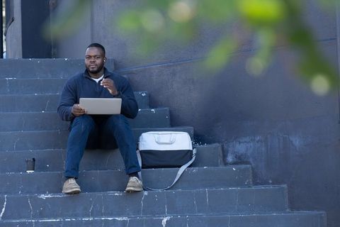 African american man working remotely on laptop while sitting on urban concrete steps