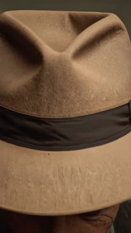 Vertical close-up of senior man in fedora lowering and raising head, vintage contemplative portrait