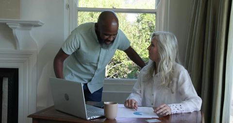 Senior couple reviewing finances in bright home office with laptop and pie chart