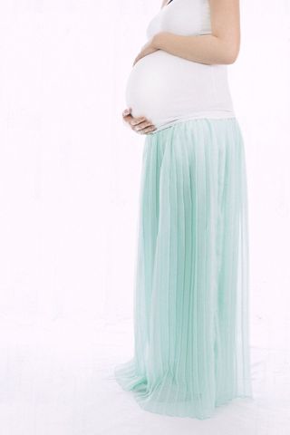 Pregnant woman touching belly in light green skirt