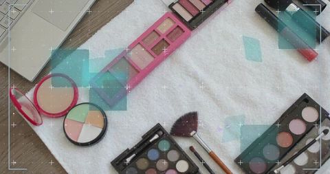 Beauty flatlay featuring pink eyeshadow palette, fan brush, compacts on white towel, lipgloss
