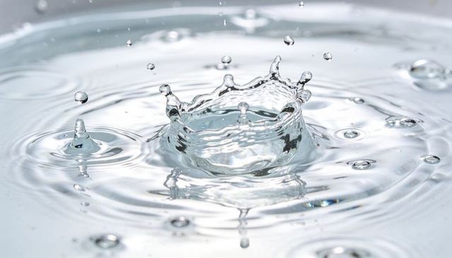 Crown splashing water droplet creating circular ripples with reflective highlights