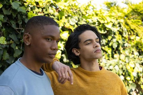 Diverse young men leaning by ivy hedge wearing mustard sweater and blue sweatshirt