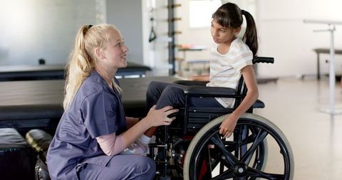 Caregiver Assisting Young Girl in Wheelchair during Therapy Session
