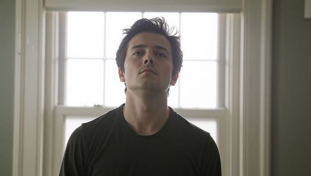 Contemplative young man standing backlit by window looking upward, moody interior portrait