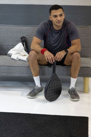 Athlete resting on sofa holding paddle racket and towel in sports lounge