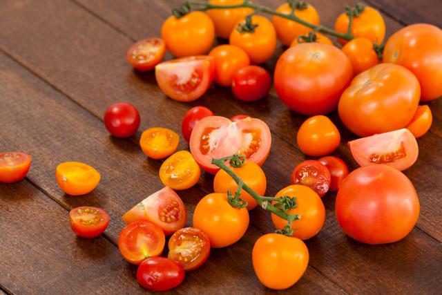 Assorted fresh tomatoes, including cherry and heirloom varieties, scattered on a wooden table. Ideal for use in food blogs, healthy eating promotions, organic produce advertisements, and cooking websites.