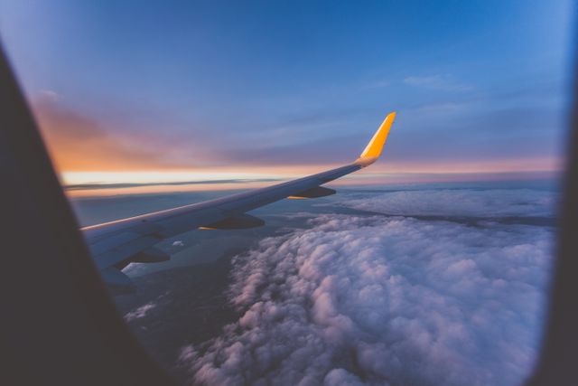 This in-flight view captures the airplane wing soaring above fluffy clouds during a beautiful sunset. Ideal for travel blogs, airline advertisements, aviation websites, and personal photo collections to evoke a sense of adventure and wanderlust.