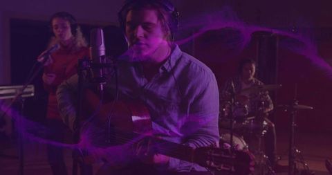 Lead singer singing and playing acoustic guitar in recording studio with purple lighting