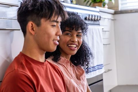 Mixed-race couple sitting on kitchen floor smiling and sharing warm candid morning moment