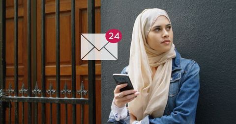 Woman in hijab holding phone checking messages outdoors