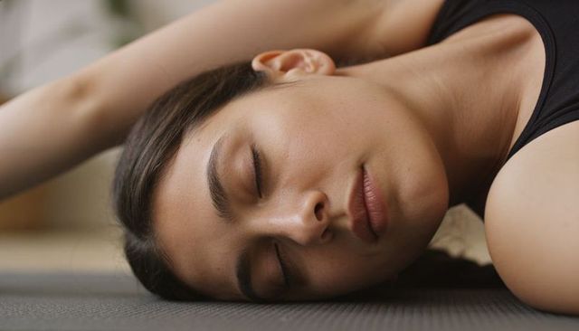 Young woman resting on yoga mat practicing mindfulness and gentle stretching at home