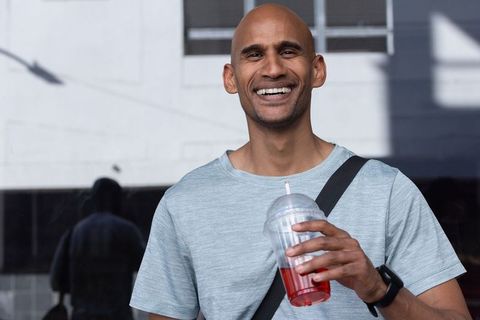 Smiling african american man holding cold red drink cup standing on urban sidewalk