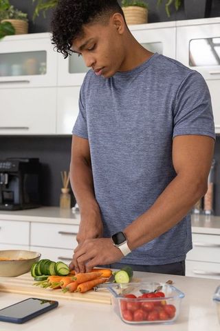 Young african american man slicing cucumber and carrots on counter preparing healthy meal