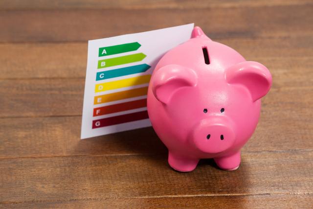 Depicts pink piggy bank alongside energy efficiency rating chart on wooden surface. Can be used for illustrating financial savings related to energy efficiency, investment strategies, or promoting green energy solutions. Ideal for financial consultations, eco-friendly campaigns, and educational materials about money management and sustainability.