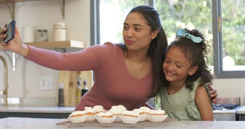 Mom and daughter taking selfie with cupcakes in bright kitchen, baking and bonding moment