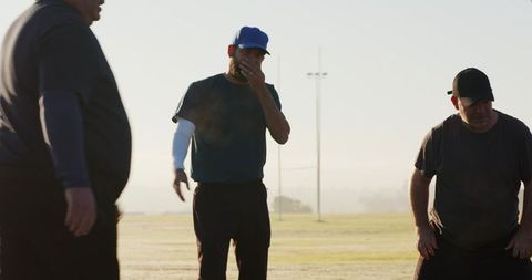 Coaches discussing strategy during early morning baseball practice on sunlit field
