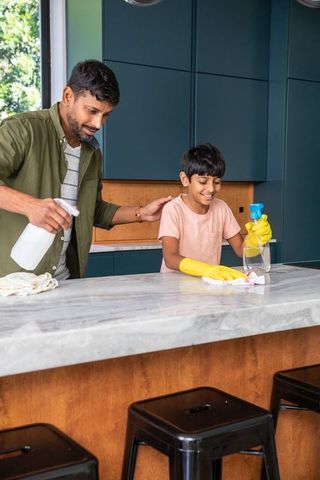 Father and son cleaning marble countertop in modern kitchen