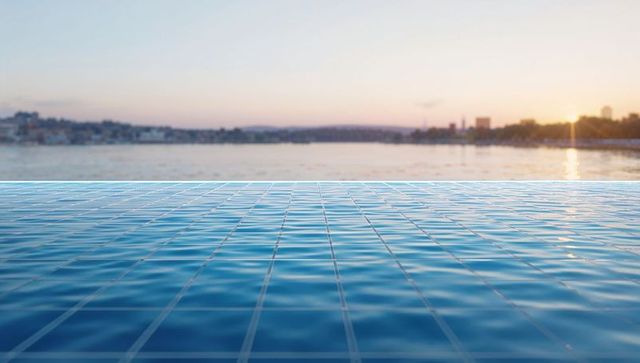 Sunset reflecting infinity pool tiles leading toward calm harbor horizon