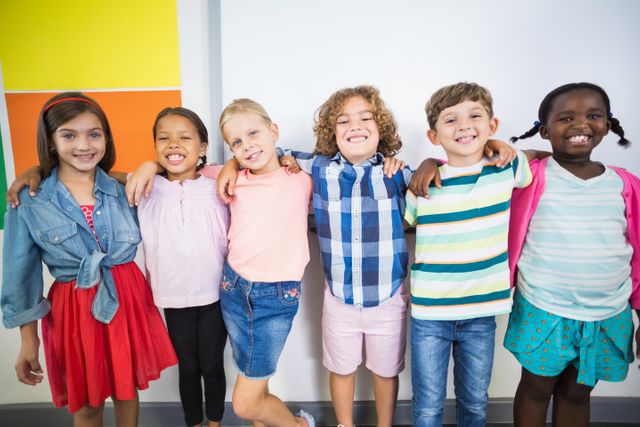 A diverse group of happy children standing together in a classroom with their arms around each other, smiling at the camera. This image can be used for educational materials, school advertisements, diversity and inclusion campaigns, and articles about childhood friendship and unity.