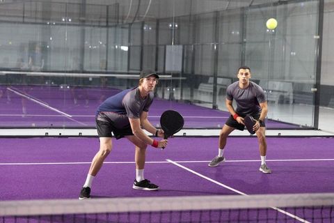 Doubles players preparing at service line on purple glass padel court tracking ball