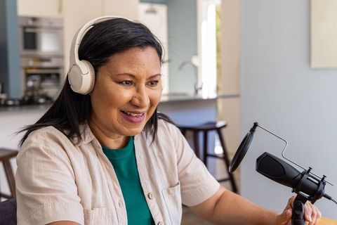 Mature woman recording home podcast wearing white headphones speaking into studio mic