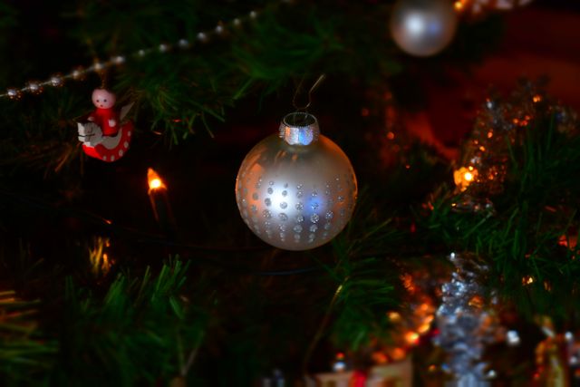 This image features a beautifully decorated Christmas tree with a focus on a silver bauble ornament and colorful holiday lights. Small additional decorations like a miniature Santa Claus add to the festive atmosphere. This image is perfect for use in holiday greeting cards, seasonal adverts, or blog posts celebrating the Christmas season.