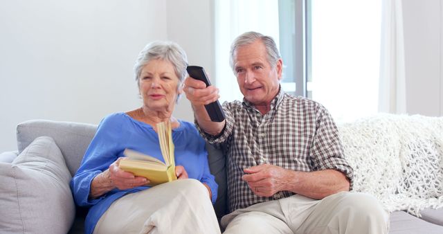 Cute elderly couple reading or watching TV sitting on sofa