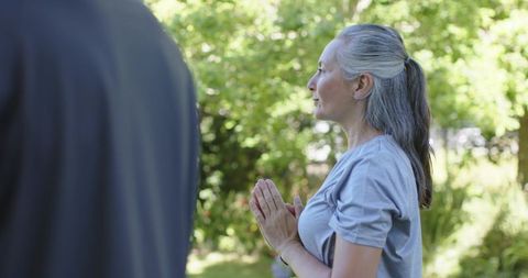 Mature woman practicing meditation outdoors with partner in sunlit garden for serenity
