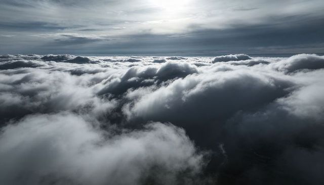 Sunlit Cloudscape Above Moody Sky, Dramatic Aerial View of Dense Rolling Clouds and Veiled Sun