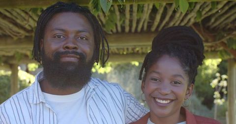 Smiling african american couple standing under wooden pergola in sunlit garden, candid portrait
