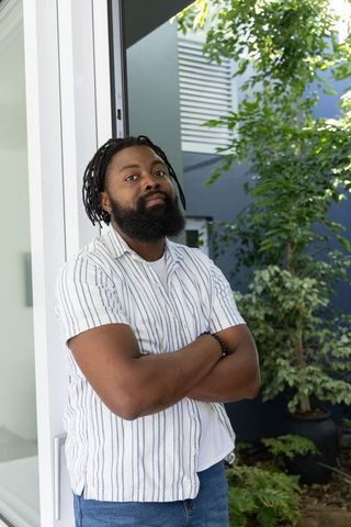 Confident african american man leaning in doorway wearing striped shirt and dreadlocks
