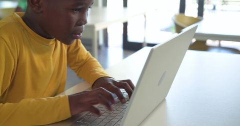 African American boy typing on laptop and focusing on homework in sunlit classroom